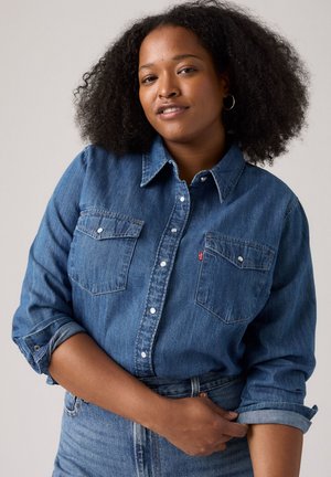 Hellblaues Denim-Hemd mit Knöpfen, zwei Brusttaschen, hochgekrempelten Ärmeln und einem Levi's-Logo-Anhänger auf der linken Tasche. Weiche Textur, lässiges Design.