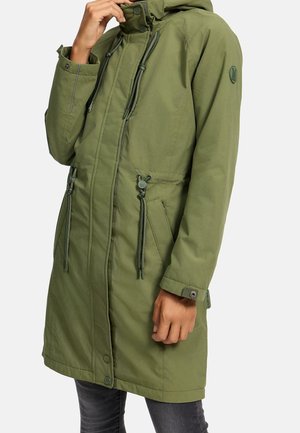 Long manteau parka vert avec zip et boutons-pression, cordons ajustables à la taille, poignets boutonnés et capuche, porté par une personne en jean foncé.