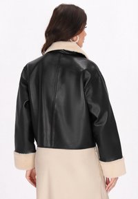 Giacca in pelle nera con un design corto, dotata di un colletto e polsini in pelliccia sintetica beige. Tessuto liscio con una cucitura posteriore pulita.