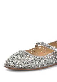 Zapato plano plateado con punta redondeada, adornado con strass claros y una tira única a lo largo del empeine. Parte superior texturizada y diseño recortado.