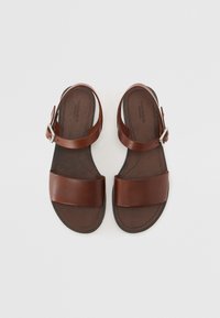 Brune lærsandaler med to brede stropper, spænde lukning og en struktureret sål, med flad sål og minimalistisk design.