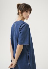 Jeans obleka v temno modri barvi, ohlapen kroj s kratkimi rokavi, surovi robovi, stranske razpoke in vidni zadrgo na hrbtu. Preprosta, moderna zasnova.