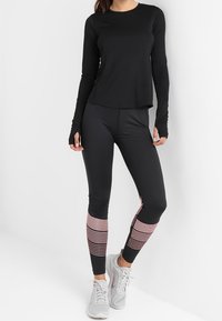 Czarna bluzka z długim rękawem w połączeniu z czarnymi legginsami z różowymi poziomymi paskami na dolnej części nóg. Uzupełniona szarymi butami sportowymi.