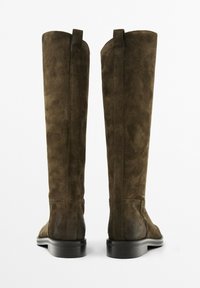 Bottes hautes en daim marron foncé, avec une texture lisse et un bout arrondi. Dotées d'une semelle plate noire et de deux tirettes en haut.