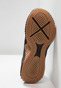 Sulan av en sko med strukturerad brun och svart gummi som har cirkulära greppmönster och en X-formad ränna över framfoten och hälen.