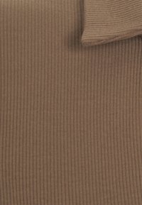 Gros plan sur un tissu en tricot côtelé marron clair avec un bord replié, montrant une fine texture verticale et des détails de matériau doux.