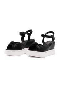 Sandali con zeppa nera, dettagli annodati sul davanti, punta aperta e cinturino regolabile. Caratterizzati da una suola piattaforma bianca con marchio. Tessuto in pelle liscia.