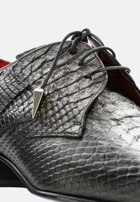 Schwarzer strukturiertes Leder-Schuh mit einem Schlangenhautmuster, ausgestattet mit einer spitzen schwarzen Akzent und Schnürsenkeln auf einem roten Innenraum.