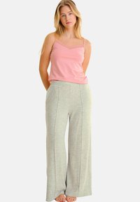 Top sans manches rose avec bord en dentelle, associé à un pantalon de survêtement ample gris clair avec des plis à l'avant et une texture douce.