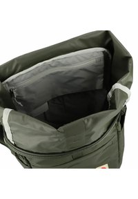 Mochila verde con tapa enrollable que presenta un exterior texturizado, forro gris y un bolsillo interior con cremallera para mayor organización. Cierre de cremallera y correa ajustable.