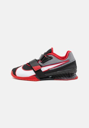 Chaussure d'haltérophilie basse en noir, blanc, rouge et gris avec une semelle épaisse et deux sangles noires pour un maintien sécurisé.