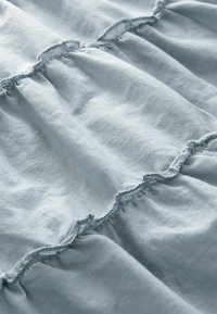Weiches, hellblaues Gewebe mit zarten, horizontally verlaufenden Rüschennähten, die Textur und sanfte Falten zeigen.