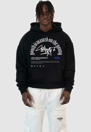 Black hoodie with white graphic text and design on the front. Features a drawstring hood and long sleeves. Worn with white cargo pants.