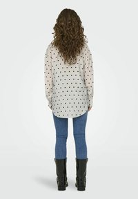 Langemouwen shirt met een stippenpatroon in het zwart op een lichte achtergrond, gecombineerd met donkerblauwe jeans en zwarte laarzen tot de knie.