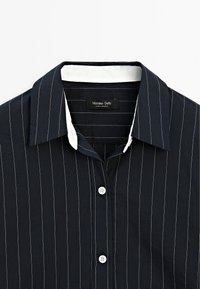 Navy blue striped shirt with a white collar, made of soft fabric. Features a button-up design and small white buttons at the front.