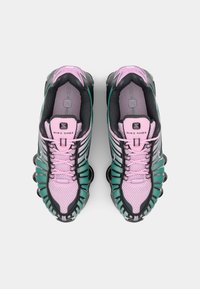 Sneakers Nike Shox w kolorze czarnym, turkusowym i różowym. Charakteryzują się materiałem z siateczki, wyraźnym systemem sznurowania oraz widocznymi kolumnami pochłaniającymi wstrząsy.