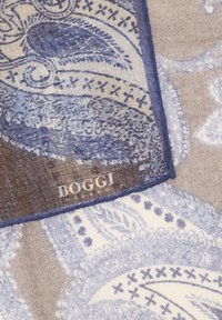 Tessuto con intricatissimi motivi paisley blu e beige, che mostra un angolo piegato con il nome del marchio "ROGGI" ricamato in bianco.