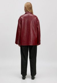 Rode leren oversized jas met een gladde textuur, een klassieke kraag en verlaagde schouders. Draag het met zwarte, wijde broek en enkellaarsjes.