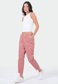 Lichtroze corduroy broek met een ontspannen pasvorm, met zijzakken en een knoopsluiting. Gepaard met een strakke witte tanktop en sneakers.