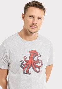 T-shirt gris avec un grand design de pieuvre rouge portant un chapeau de marin bleu. Manches courtes et encolure ronde classique.