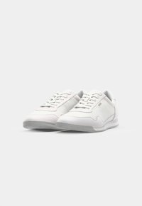 Chaussures de sport blanches avec une tige en cuir lisse, un bout rond, un design à lacets et un marquage subtil sur le côté. Semelle en caoutchouc.