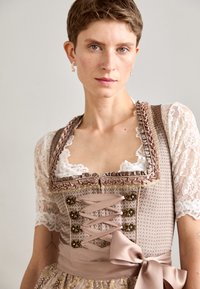 Tenue traditionnelle avec un corsage ajusté en rose pâle et des manches en dentelle, présentant des détails floraux complexes, des accents en ruban et une jupe texturée.
