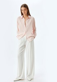 Camisa de botones rosa claro con mangas largas, combinada con pantalones blancos holgados. La camisa tiene un corte relajado y una textura suave.