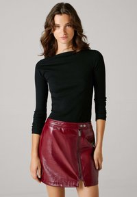 Μαύρο μακρυμάνικο κορμάκι με ριμπ ύφανση, συνδυασμένο με μίνι δερμάτινη φούστα σε γυαλιστερό μπορντό χρώμα, με φερμουάρ στο πλάι και κούμπωμα μ�ε κουμπί.
