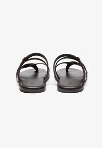 Brown leather sandals with multiple slim straps, flat sole, and minimalistic design. Features a smooth texture and subtle branding on the footbed.