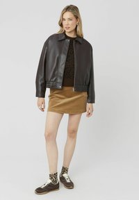 Veste en cuir marron avec un col haut, associée à un pull à imprimé léopard noir et à une jupe en velours côtelé beige. Baskets marron avec des chaussettes léopard.