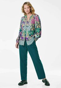 Camicia a maniche lunghe con un motivo multicolore e una vestibilità ampia, abbinata a pantaloni larghi teal scuro e mocassini neri spessi.