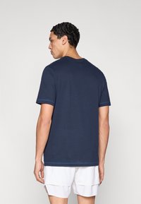 Μπλε κοντομάνικη μπλούζα με στρογγυλή λαιμόκοψη, κατασκευασμένη από απαλό ύφασμα, με αντίθετες μπλε ραφές στα μανίκια και το τελείωμα.