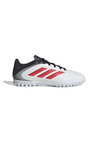 Zapato de fútbol blanco con acentos negros y tres rayas rojas. Presenta una superficie texturizada, punta redondeada y una suela de goma con múltiples tacos.