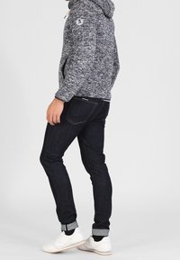 Melerad grå hoodie med dragsko, mörkblå jeans med uppvikta fållar och vita sneakers. Slim fit med subtila sömnadsdetaljer.