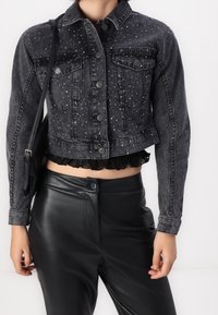 Czarna skórzana kurtka krótka z srebnymi ćwiekami, dwoma przednimi kieszeniami, zapięciem na guzik i dołem wykończonym koronką. Noszona z czarnymi skórzanymi spodniami.