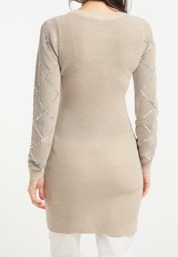 Beige ribbat stickad klänning med långa ärmar, med en strukturerad mönster och dekorativa detaljer längs ärmarna.