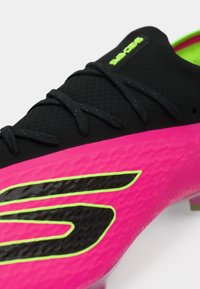 Černý fotbalový kopačka s růžovými a zelenými akcenty, texturovaným povrchem a černými tkaničkami. Obsahuje výrazné logo S v černé a zelené barvě.