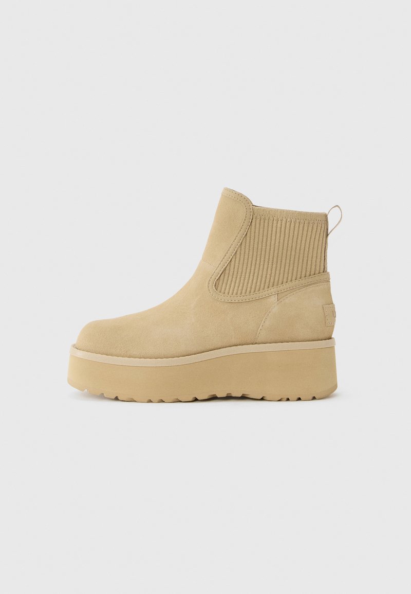 Beige semsket ankelstøvel med tykk plattformsåle og ribbet elastisk sidepanel, sett fra utsiden mot en ensfarget bakgrunn.