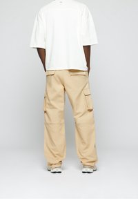 T-shirt ample en coton blanc avec épaules tombantes, associée à un pantalon cargo beige doté de multiples poches et d'une silhouette décontractée.