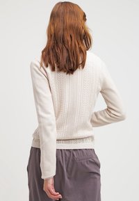 Lichtbeige gebreide trui met gestructureerde patronen en aansluitende mouwen. De achterkant heeft een ontwerp met subtiele verticale lijnen en geribbelde accenten.