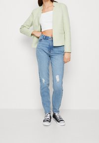 Jasnozielona krótka marynarka, biała bluzka krótkiego kroju, zniszczone jasnoniebieskie dżinsy i czarne wysokie trampki z białą podeszwą.