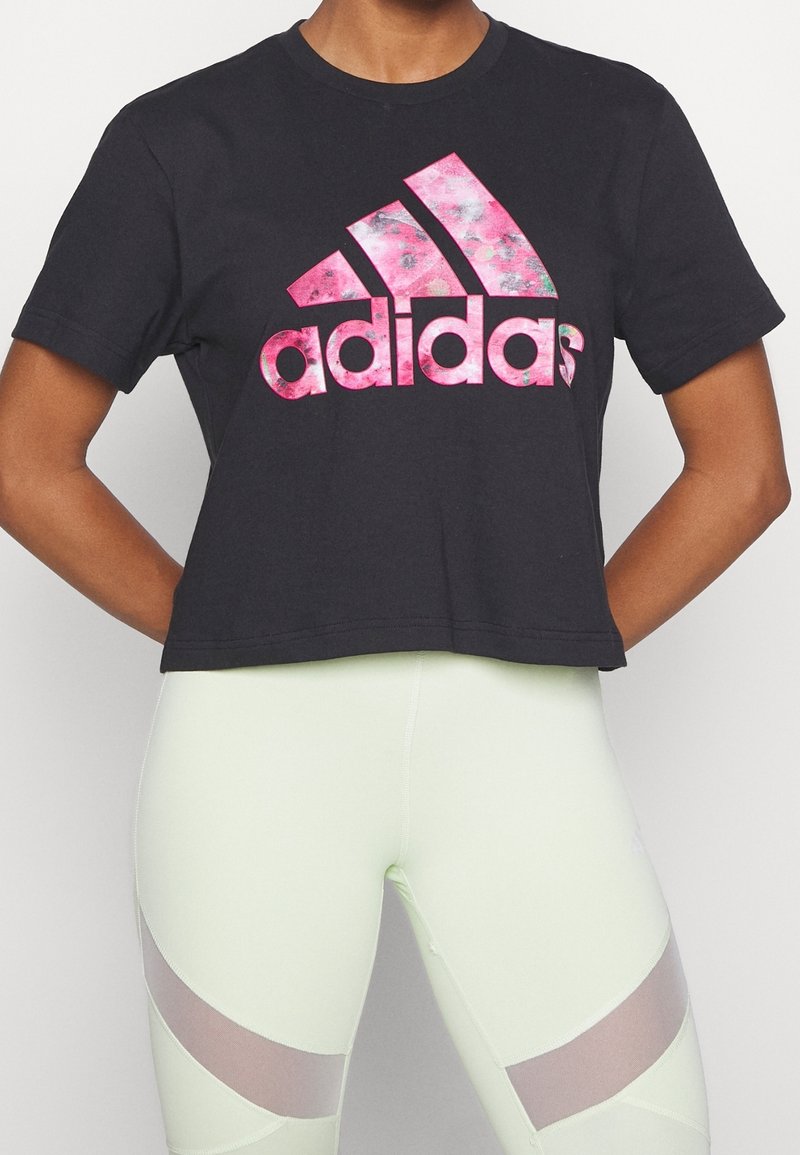 Personne portant un t-shirt court noir avec un logo Adidas rose et des leggings clairs avec des panneaux en maille sur les cuisses.