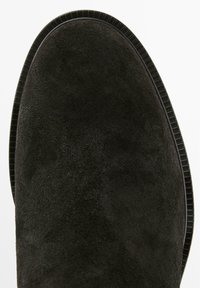 Punta di stivale in suede nero con punta rotonda e bordo della suola testurizzato visibile su sfondo bianco.