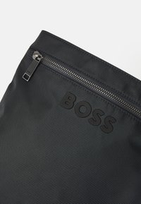 Borsa nera in nylon con superficie testurizzata, chiusura con zip e logo "BOSS" in rilievo. Design minimalista con accenti eleganti.