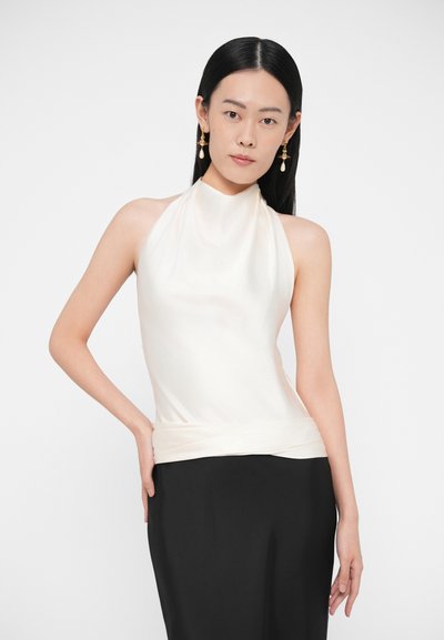 Krémový horný diel na zaväzovanie za krk s preloženým dizajnom, jemnou textúrou a priliehavým pásom. Kombinovaný s čiernou sukňou. Zlaté náušnice s perlou.