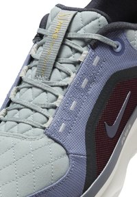 Sneakers Nike avec une tige matelassée bleu clair, des accents bleu marine foncé, un panneau latéral bordeaux, des lacets gris et une semelle intermédiaire blanche proéminente.