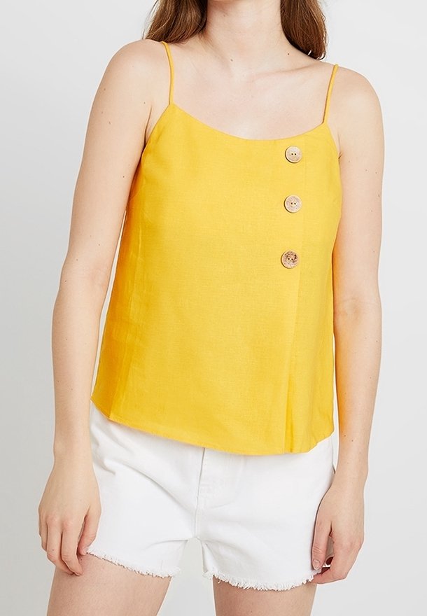 Yellow linen tank top with thin straps, a straight neckline, and three decorative buttons on the left side. Paired with white shorts.