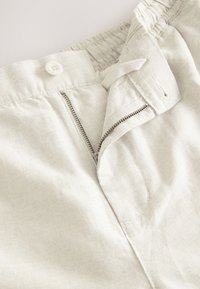 Light-colored fabric with a smooth texture, featuring a button closure and a zip fly, showcasing stitched details along the waistband.