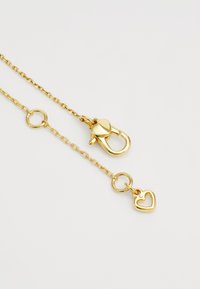 Colar de corrente dourada com fecho em forma de coração e um pequeno encantamento em forma de coração. Textura suave com elos e acentos circulares.