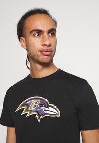 Black cotton t-shirt with a large purple and white Baltimore Ravens logo on the front, featuring bold lines and smooth texture.